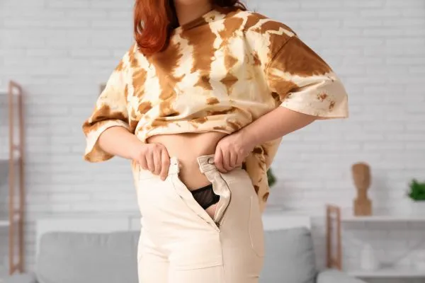 Image of woman trying to do her trousers up after pregnancy weight gain Milngavie