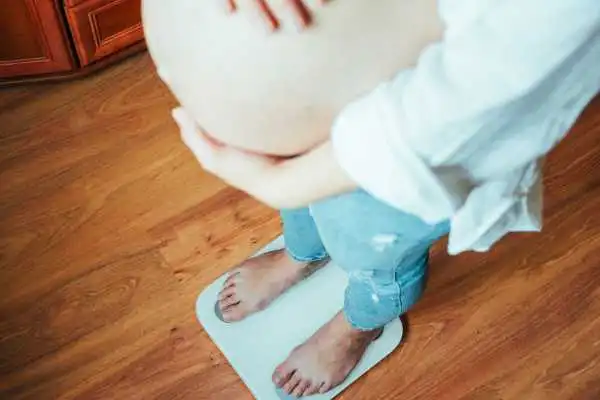 Image of woman weighing herself and experiencing weight gain through pregnancy Milngavie
